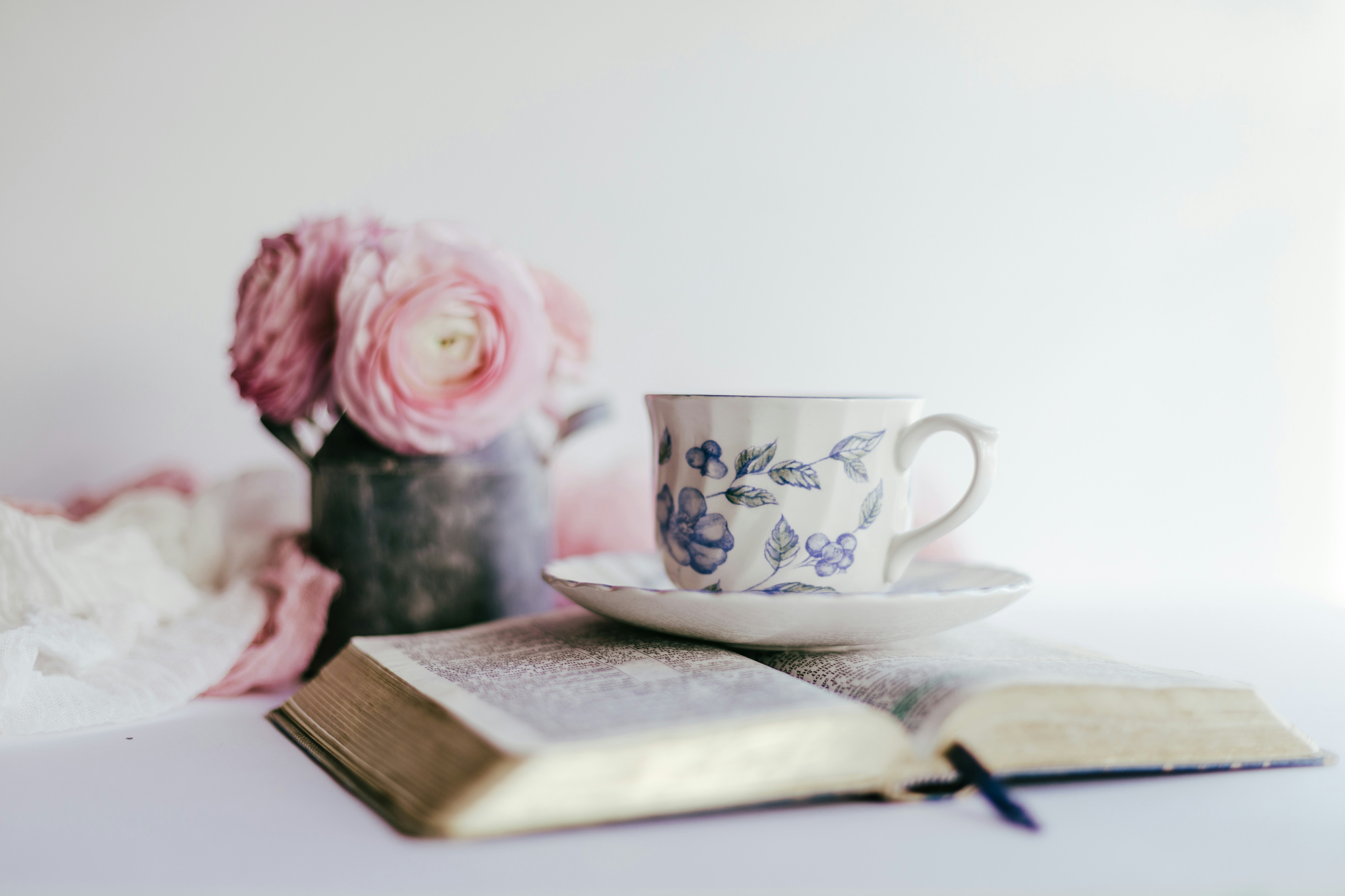 Open Bible with teacup and pink ranunculus on a soft cream background